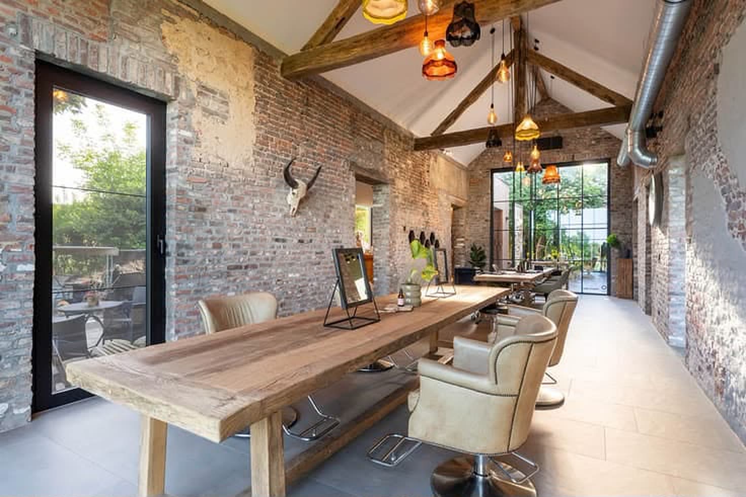 Lange massief houten werktafel voor een bakstenen muur, onder zichtbare eiken spanten.