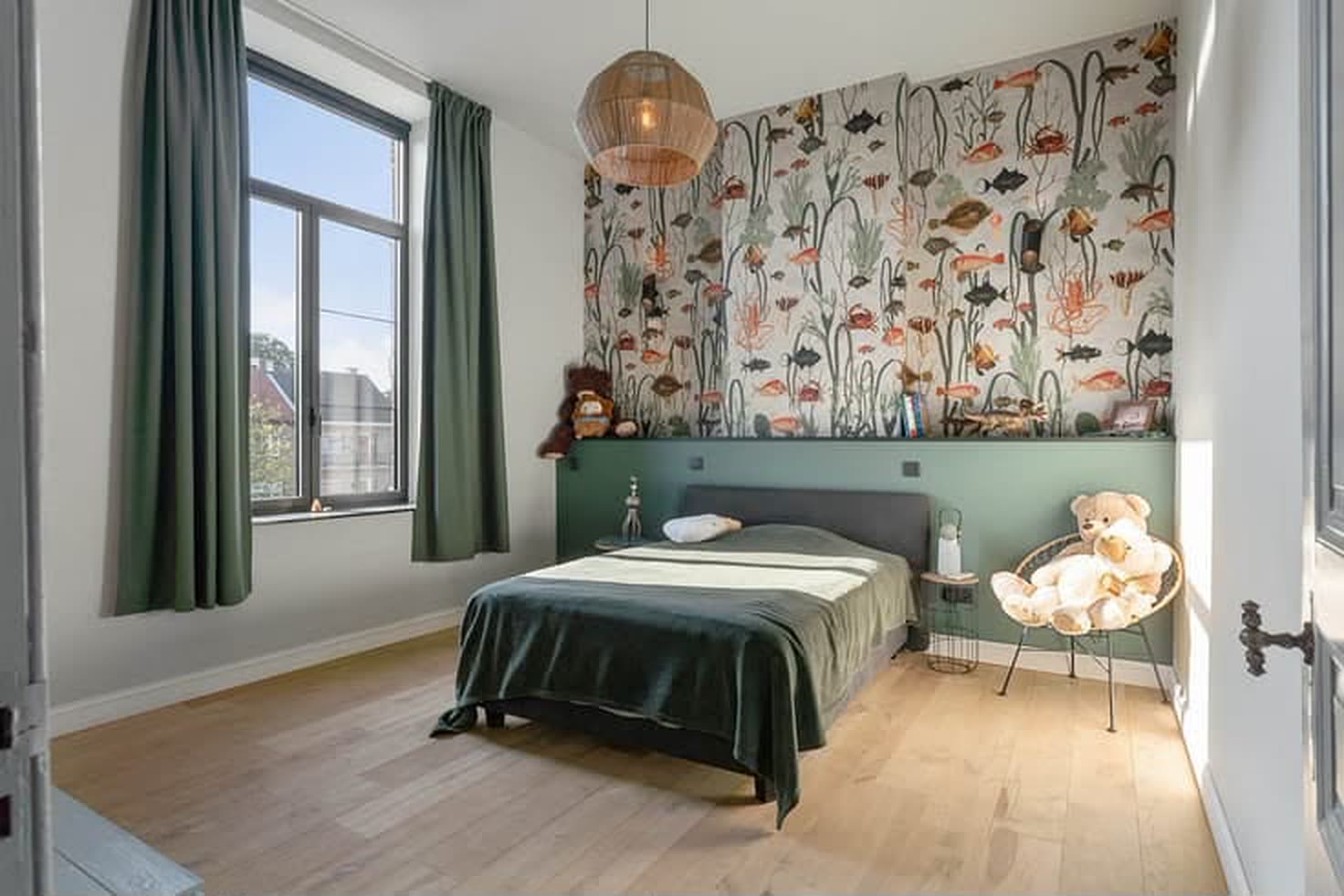 Kinderslaapkamer met groen bed, illustratief behang en groene gordijnen.