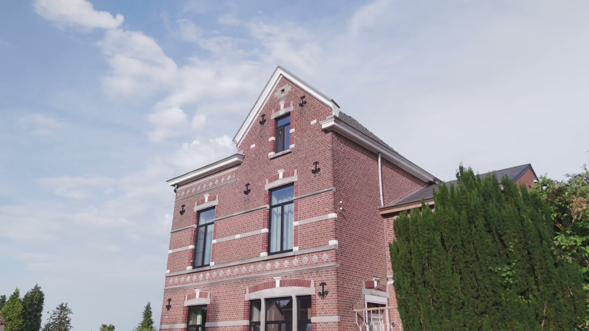 Het herenhuis van onderaf gezien: bakstenen gevel met sierbanden, muurankers en de statige puntgevel tegen een open lucht.